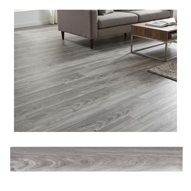 Gray wood-look laminate or vinyl plank flooring shown installed in a living room setting with a sofa, coffee table, and rug, plus a close-up material sample strip at the bottom.