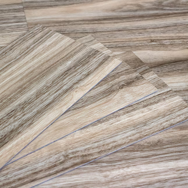 Close-up of several overlapping wood-look flooring samples with a light tan and medium brown grain pattern on a white background.